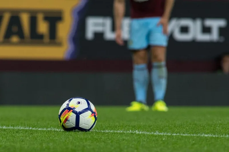A close-up of a football on a green grass pitch, suitable for a Premier League match.