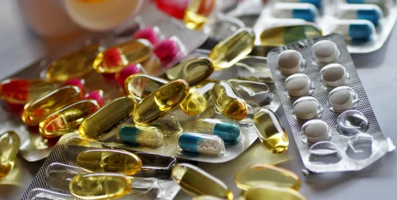 Eine Reihe weisser Tabletten und Kapseln, die auf einer Oberfläche liegen und verschwommen im Hintergrund.