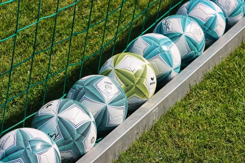 Mehrere Fussbälle liegen auf einem grünen Rasenfeld, bereit für ein Fussballtraining.