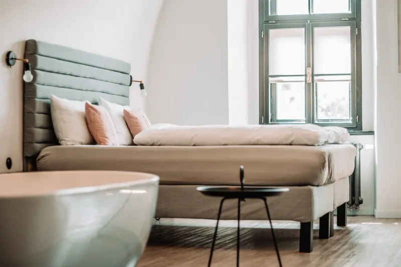 Ein helles Hotel-Schlafzimmer mit einem Doppelbett und Fenstern.