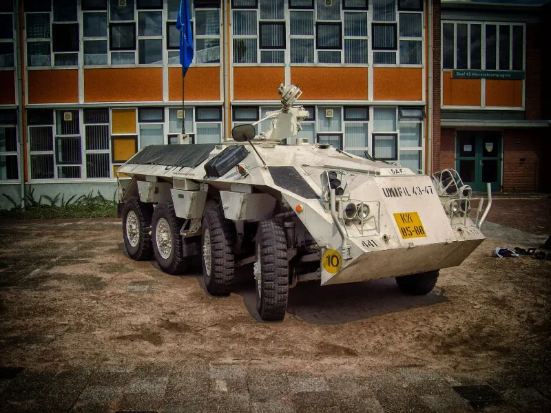 Ein weisses Militärfahrzeug mit einem blau-weissen UN-Logo an der Seite, das auf einer staubigen Strasse fährt.