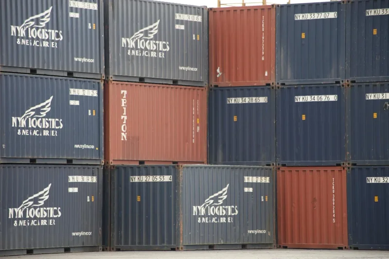 Zahlreiche bunte Frachtcontainer stapeln sich in einem grossen Hafen, Kräne sind im Hintergrund sichtbar.