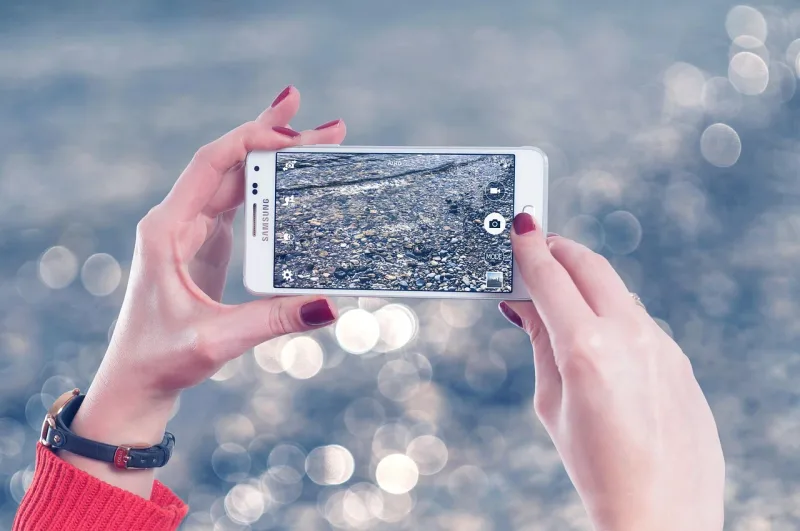 Eine Person hält ein Smartphone und nutzt die Kamerafunktion, mit unscharfem Hintergrund.