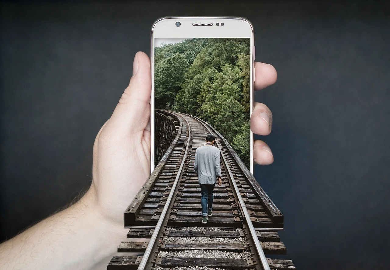 Smartphone neben Bahngleisen an einer Zugstrecke.